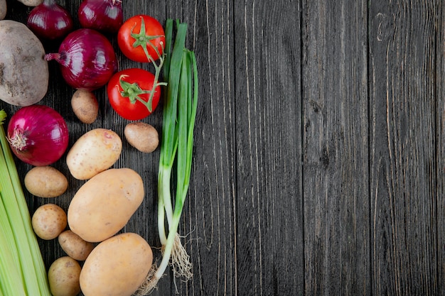 Vista superior de verduras como cebolla apio patata tomate y cebolleta en el lado izquierdo y fondo de madera con espacio de copia