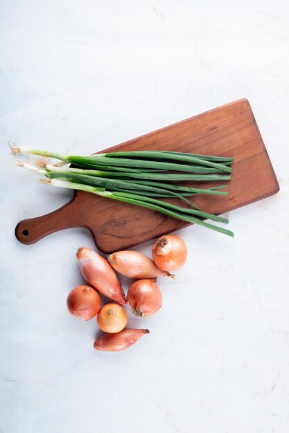 Vista superior de verduras como cebolla verde en tabla de cortar y chalota sobre fondo blanco con espacio de copia