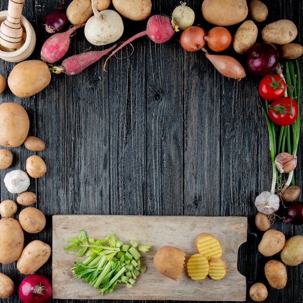 Vista superior de verduras como cebollín rábano cebolla ajo con apio cortado y patata en tabla para cortar sobre fondo de madera con espacio de copia