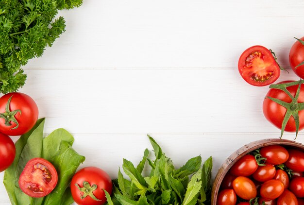 Vista superior de verduras como cilantro, tomate, espinacas, hojas de menta verde sobre superficie de madera con espacio de copia