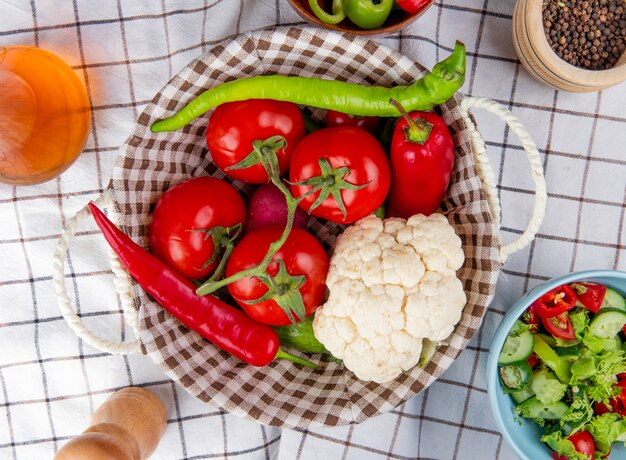 Vista superior de verduras como coliflor de rábano pimiento tomate en la cesta con mantequilla ensalada de vegetales pimienta negra sobre fondo de tela escocesa