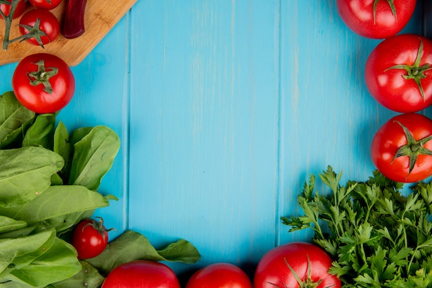 Vista superior de verduras como espinacas tomate cilantro con cuchillo en la tabla de cortar en azul con espacio de copia