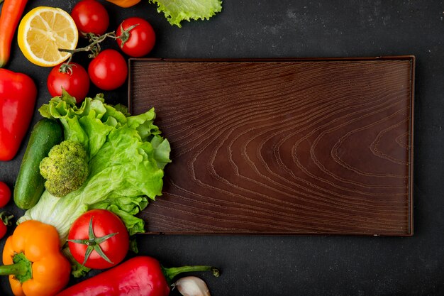 Vista superior de verduras como lechuga brócoli tomate pepino con limón y tabla de cortar sobre fondo negro