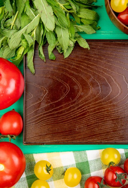 Vista superior de verduras como menta verde deja tomates alrededor de la bandeja vacía en la superficie verde