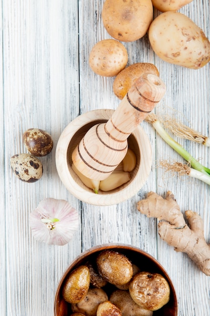 Vista superior de verduras como patata huevo ajo jengibre con patata al horno y trituradora de ajo sobre fondo de madera con espacio de copia
