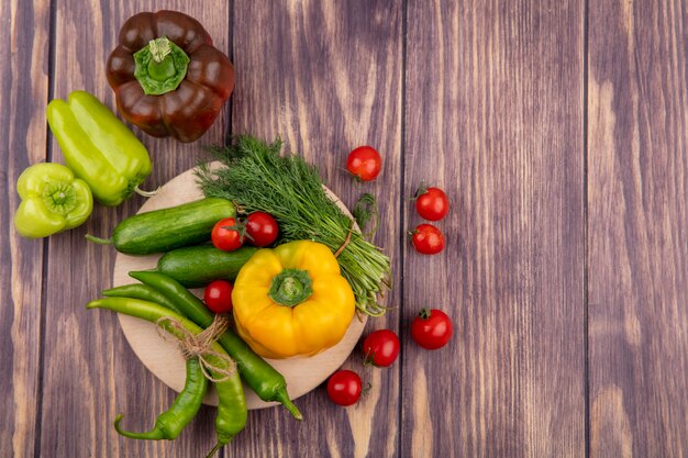 Vista superior de verduras como pepino pimiento eneldo tomate en tabla de cortar y en superficie de madera