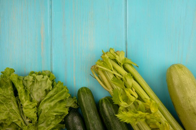 Vista superior de verduras como pepinos, lechuga, calabacín y apio aislado en una pared de madera azul con espacio de copia