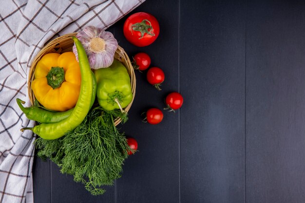Vista superior de verduras como pimienta eneldo ajo en canasta con tomates y tela escocesa sobre superficie negra