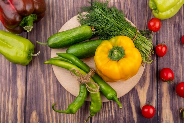 Vista superior de verduras como pimiento eneldo pepino en tabla de cortar con tomates en superficie de madera