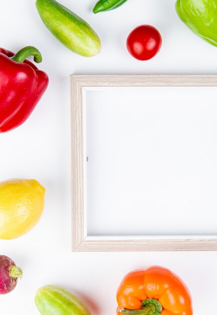 Vista superior de verduras como pimiento pepino rábano tomate con marco sobre superficie blanca con espacio de copia