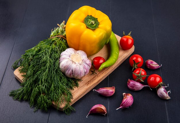 Vista superior de verduras como pimiento tomate ajo bulbo manojo de eneldo en tabla de cortar con dientes de ajo en superficie negra