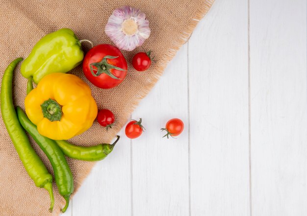 Vista superior de verduras como pimiento tomate ajo sobre tela de saco y superficie de madera