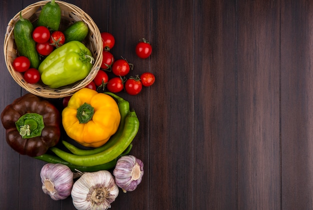 Vista superior de verduras como pimiento tomate pepino ajo en canasta y sobre superficie de madera