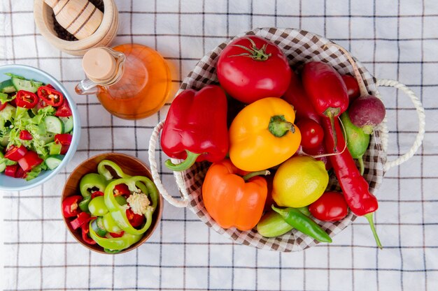 Vista superior de verduras como pimiento, tomate, pepino en una cesta con ensalada de verduras, mantequilla derretida y trituradora de ajo sobre una superficie de tela escocesa