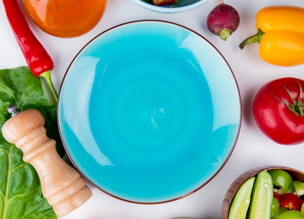 Vista superior de verduras como rábano pimiento tomate con mantequilla y dejar con plato vacío sobre superficie blanca