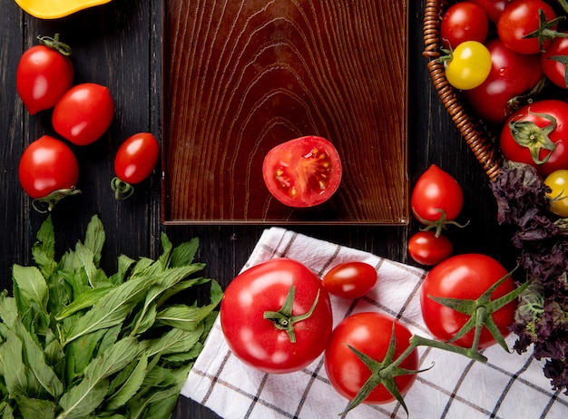 Vista superior de verduras como tomate albahaca en canasta y corte de tomate en bandeja con hojas de menta verde sobre superficie de madera