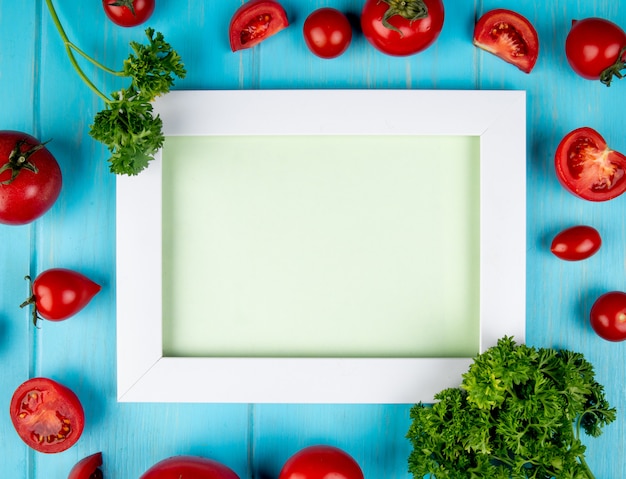 Vista superior de verduras como tomate y cilantro alrededor del tablero en azul con espacio de copia