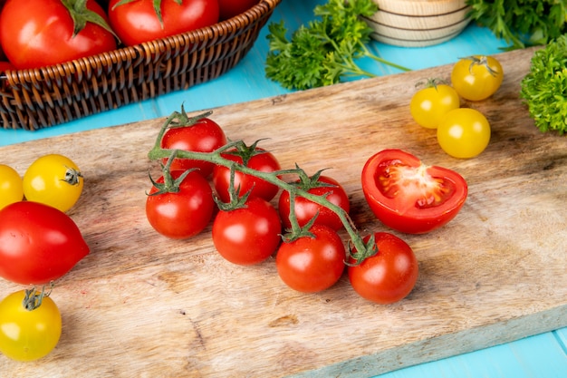 Vista superior de verduras como tomate cilantro en tabla de cortar con tomates trituradores de ajo en superficie azul