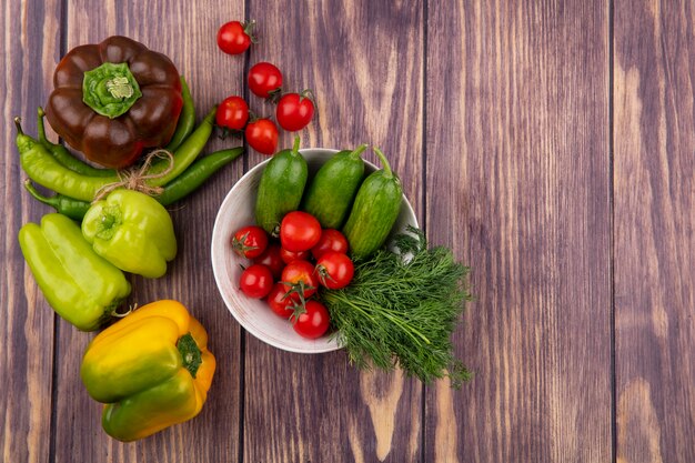 Vista superior de verduras como tomate eneldo pepino en un tazón con pimientos sobre superficie de madera