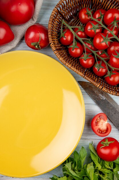 Vista superior de verduras como tomate hojas de menta verde con cuchillo y plato vacío en madera