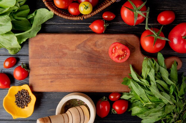 Vista superior de verduras como tomate y hojas de menta verde con semillas de pimienta negra y trituradora de ajo y corte de tomate en tabla de cortar en madera