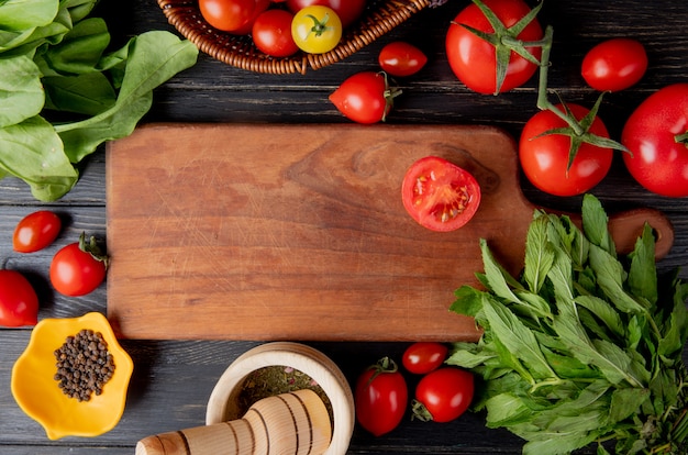 Vista superior de verduras como tomate y hojas de menta verde con semillas de pimienta negra y trituradora de ajo y corte el tomate en una tabla de cortar sobre una superficie de madera