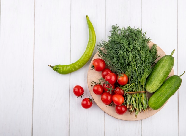 Vista superior de verduras como tomate pepino y eneldo en tabla de cortar con pimiento sobre superficie de madera