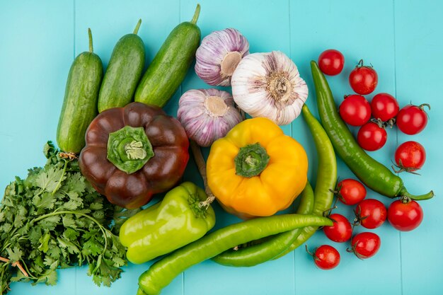 Vista superior de verduras como tomate pepino pimienta ajo y cilantro sobre superficie azul