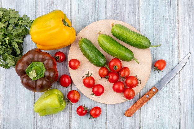 Vista superior de verduras como tomate pepino en tabla de cortar con pimienta cilantro y cuchillo sobre superficie de madera