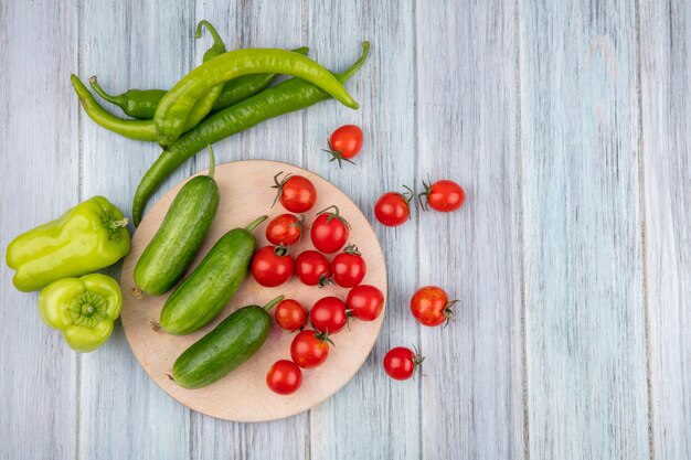 Vista superior de verduras como tomate pepino en tabla de cortar con pimiento sobre superficie de madera