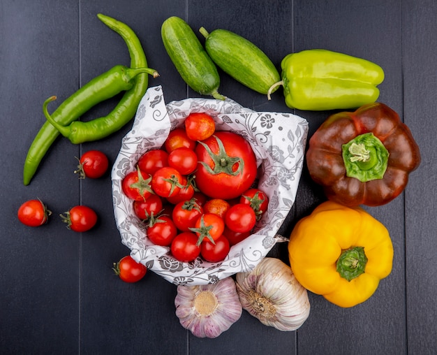 Vista superior de verduras como tomates en la cesta pepinos pimientos bulbos de ajo en superficie negra