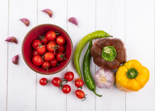 Vista superior de verduras como tomates en un tazón pimientos bulbo de ajo y dientes sobre superficie de madera