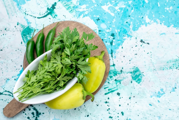 Vista superior de verduras frescas aisladas dentro de la placa junto con pimientos verdes y pimientos picantes en azul brillante, comida de producto de hoja verde