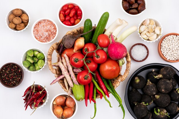 Vista superior de verduras frescas en la cesta rodeada de otros vegetales en platos y tazones blancos sobre blanco