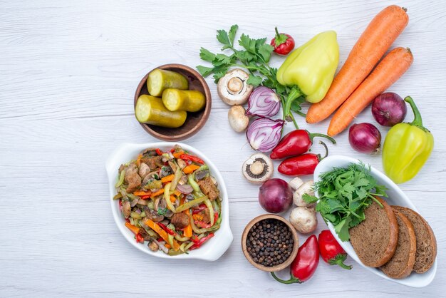 Vista superior de verduras frescas como cebollas de zanahoria pimiento con hogazas de pan y plato de carne en rodajas en el escritorio de luz, comida vegetal vitamina