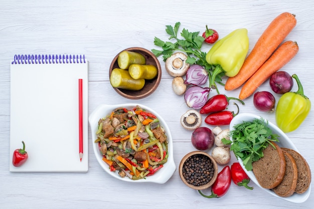 Vista superior de verduras frescas como cebollas de zanahoria con pimiento con hogazas de pan y plato de carne en rodajas a la luz, comida vegetal vitamina