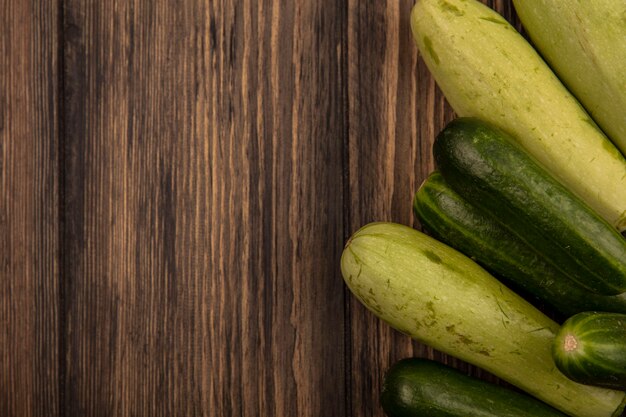 Vista superior de verduras frescas como pepinos y calabacines aislados en una pared de madera con espacio de copia