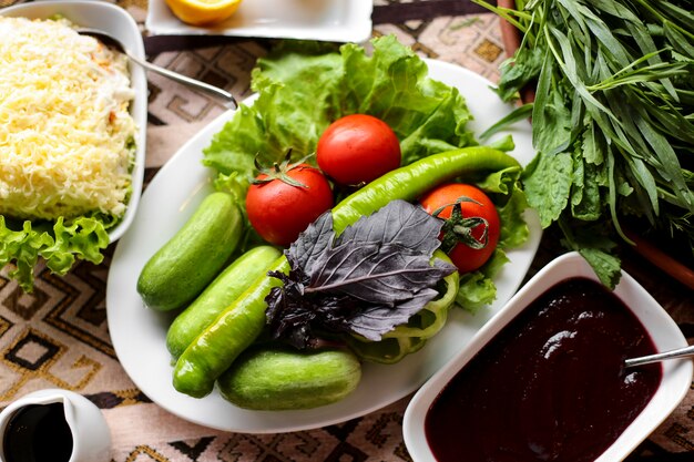 Vista superior de verduras frescas como pepinos tomates y albahaca sobre lechuga en un plato