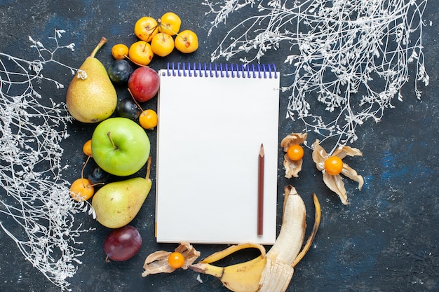 Vista superior de verduras frescas, como peras, manzana verde, cerezas amarillas, ciruelas y bloc de notas en el escritorio azul, alimentos de bayas frescas de frutas