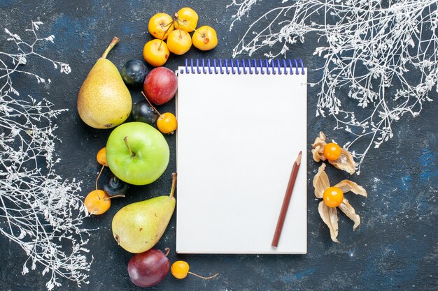 Vista superior de verduras frescas, como peras, manzana verde, cerezas amarillas, ciruelas y bloc de notas en el escritorio azul oscuro, alimentos de bayas frescas de frutas