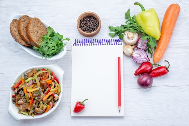 Vista superior de verduras frescas como zanahoria, cebollas y pimiento verde con rodajas de carne en un piso ligero, comida vegetal, carne de vitamina