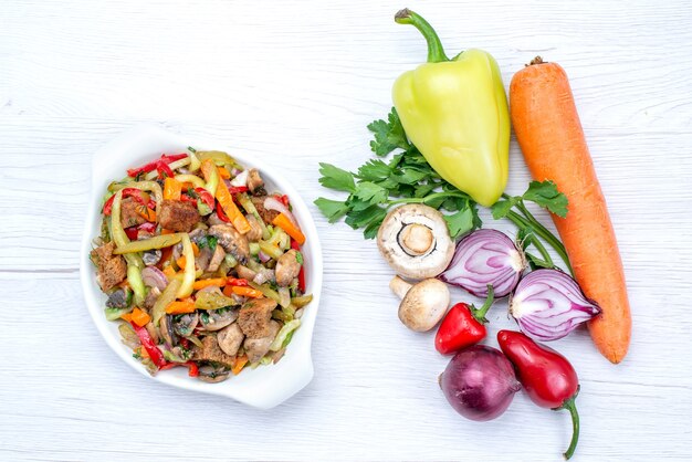 Vista superior de verduras frescas como zanahoria, cebollas verdes y pimiento verde con rodajas de carne en un escritorio de luz, comida vegetal vitamina