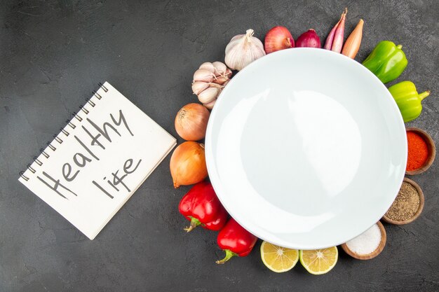 Vista superior de verduras frescas con condimentos y escritura de vida saludable sobre fondo gris