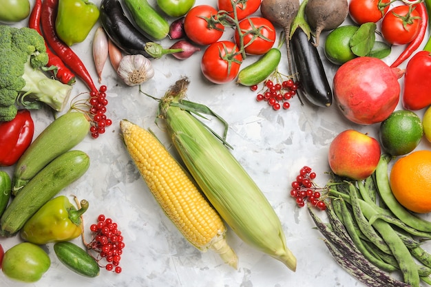 Vista superior de verduras frescas con frutas y maíz sobre fondo blanco.