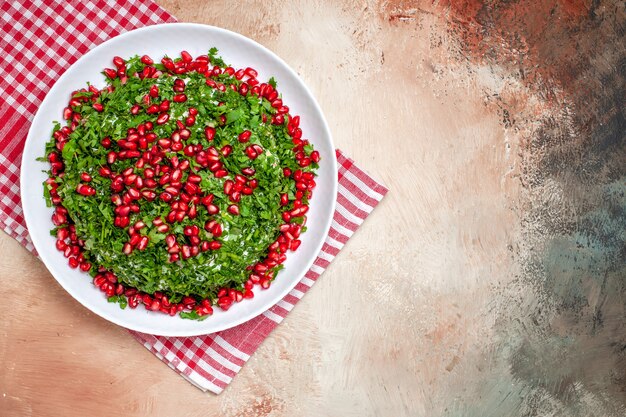 Vista superior de verduras frescas con granadas peladas en mesa de luz color verde