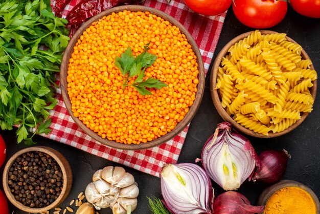 Vista superior de verduras frescas, lentejas rojas en un tazón marrón, pastas de pimienta, botella de aceite caída