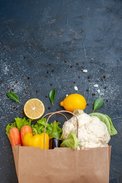 Vista superior verduras frescas limón pimiento coliflor zanahoria lechuga en bolsa de compras sobre fondo oscuro