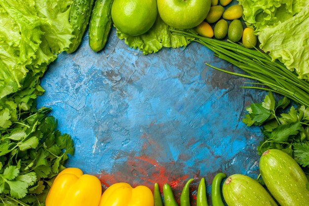 Vista superior de verduras frescas con manzanas, pepinos y otros productos sobre fondo azul.