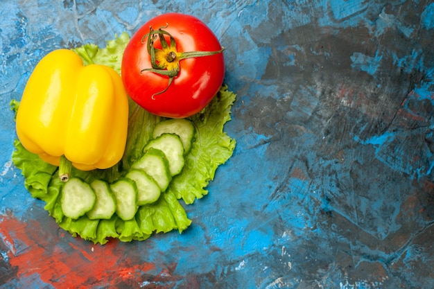 Vista superior de verduras frescas pepino tomate ensalada verde y ajo sobre fondo azul.