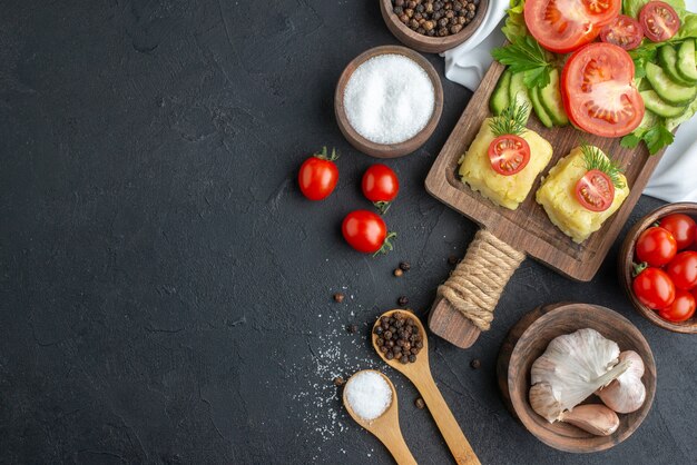 Vista superior de verduras frescas picadas y enteras en la tabla de cortar en tazones y especias en una toalla blanca en el lado izquierdo sobre una superficie negra